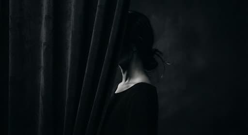 A figure partially obscured by a dark curtain